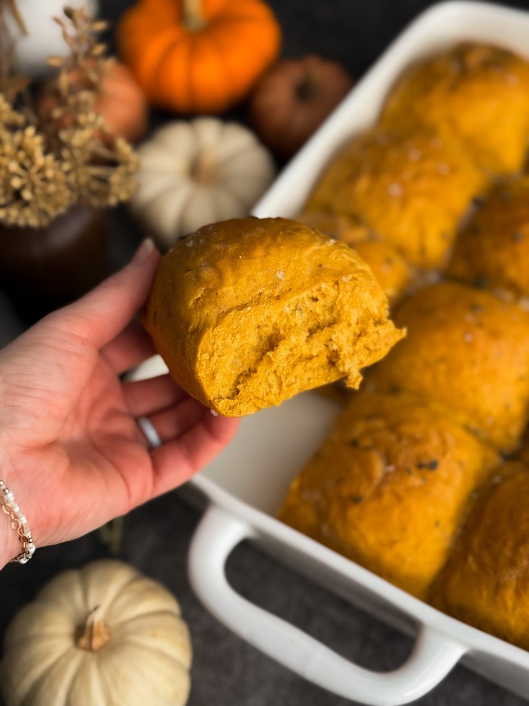 Holding a super fluffy Pumpkin Sage Dinner Roll - aka holding a super fluffy Pumpkin Dinner Roll. This recipe uses pumpkin puree and fresh sage leaves, making it unique and delicious. These Pumpkin Sage Dinner Rolls are a recipe by Christine Manes from Home-Cooked Living, a healthy recipe website.