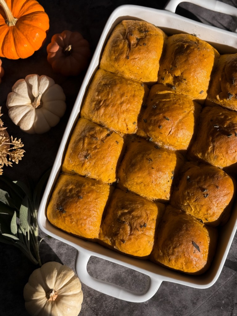 The absolute BEST pumpkin dinner rolls on Pinterest and instagram! Pumpkin Sage Dinner Rolls in a 9x13 baking dish with golden tops. These Pumpkin Sage Dinner Rolls are a recipe by Christine Manes from Home-Cooked Living, a healthy recipe website.