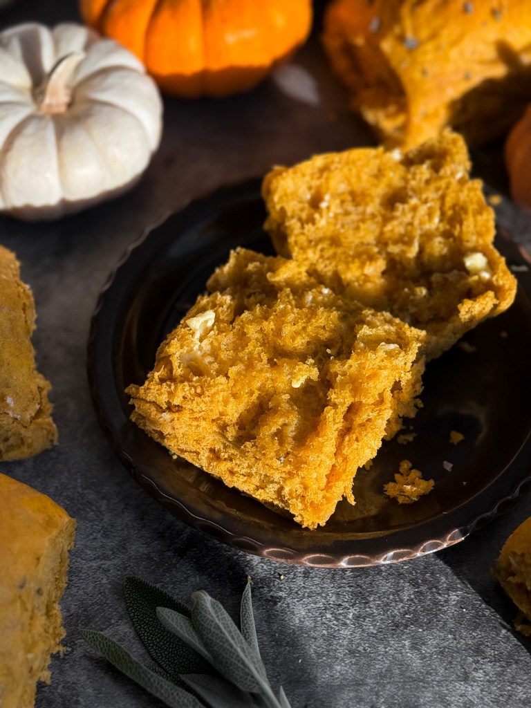 Pumpkin sage dinner roll split in half with warm, golden butter smeared on it. These Pumpkin Sage Dinner Rolls are a recipe by Christine Manes from Home-Cooked Living, a healthy recipe website.