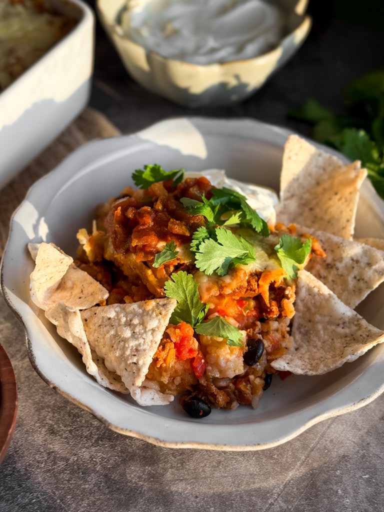 A bowl of Healthy Taco Casserole with Siete chips, sour cream, salsa, and cilantro.