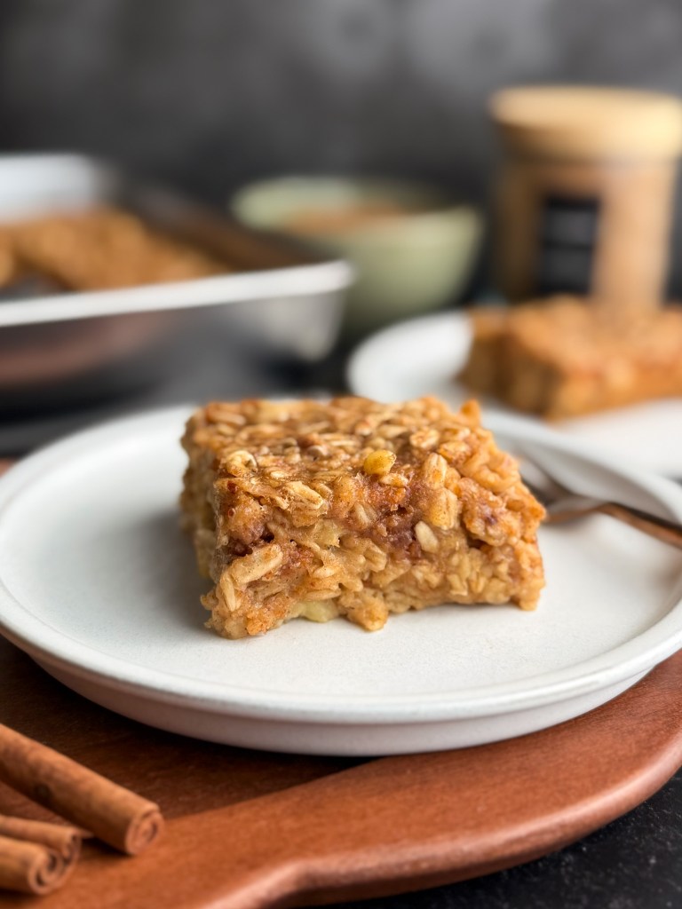 Side view of a freshly baked slice of Almond Butter Banana Baked Oatmeal on a white plate - showing a gooey, warm center. Recipe by https://homecookedliving.com.