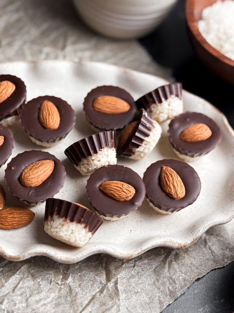 Healthy Almond Joy Cups on a beautiful ceramic dish - showcasing the coconut layered with chocolate and an almond on top.