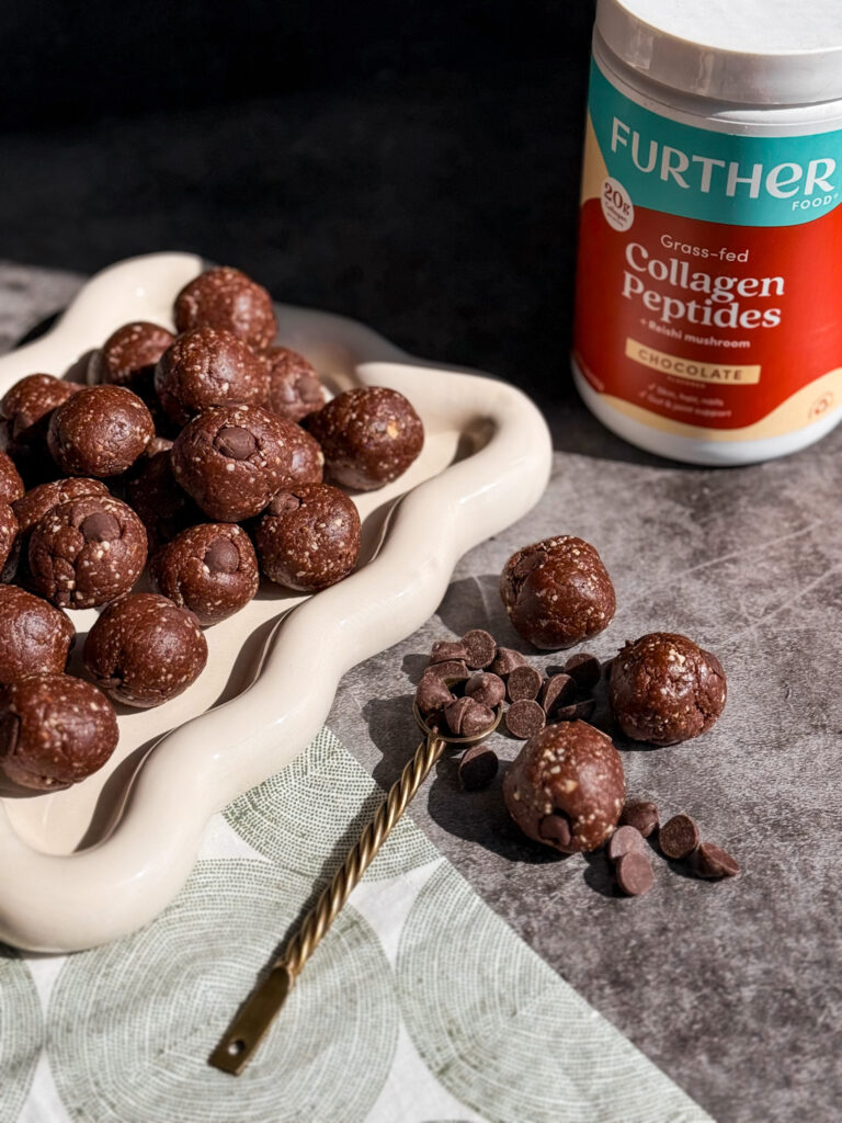 Chewy Chocolate Nourish Balls on a white platter with further food chocolate collagen peptides in the background