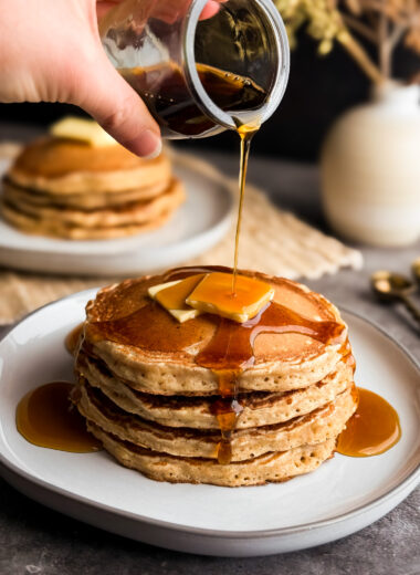 Cover photo of Fluffy Wheat Pancakes with maple syrup being poured on top