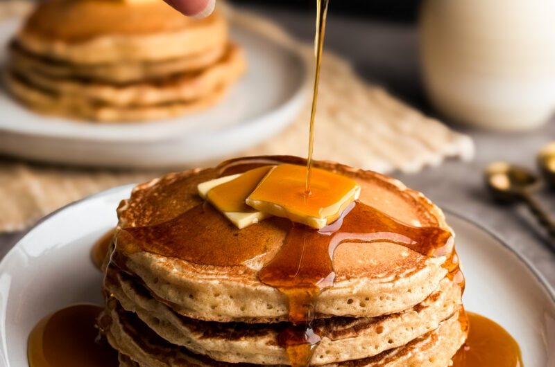 Cover photo of Fluffy Wheat Pancakes with maple syrup being poured on top