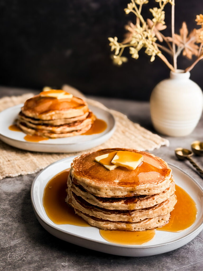 A stack of fluffy wheat pancakes with pure maple syrup and butter on top